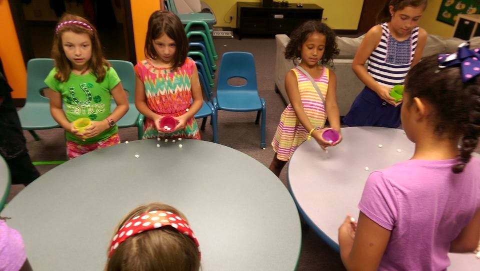 Children playing a game with cups and small objects at tables