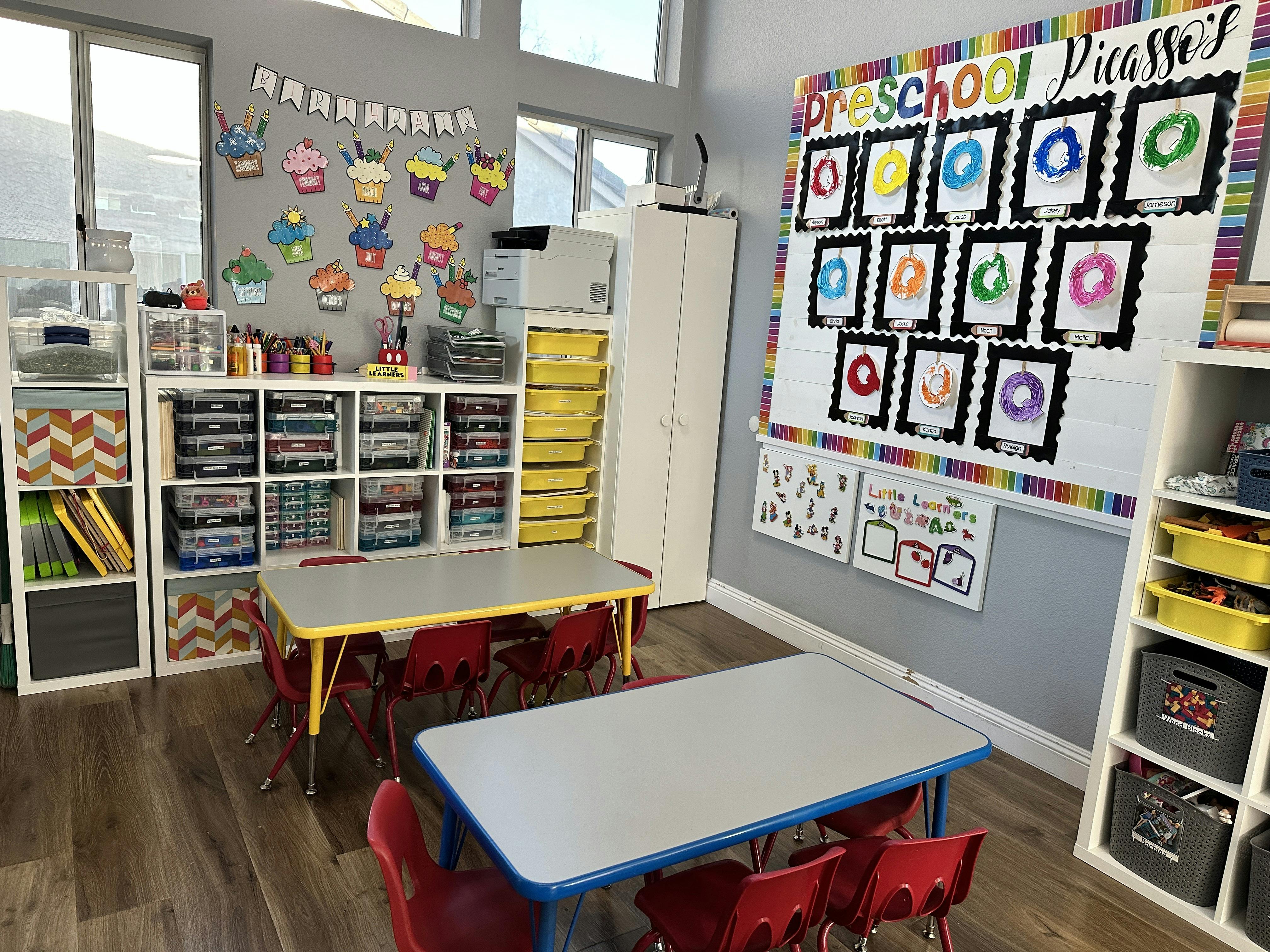 Classroom with small tables and chairs, storage shelves, and a bulletin board