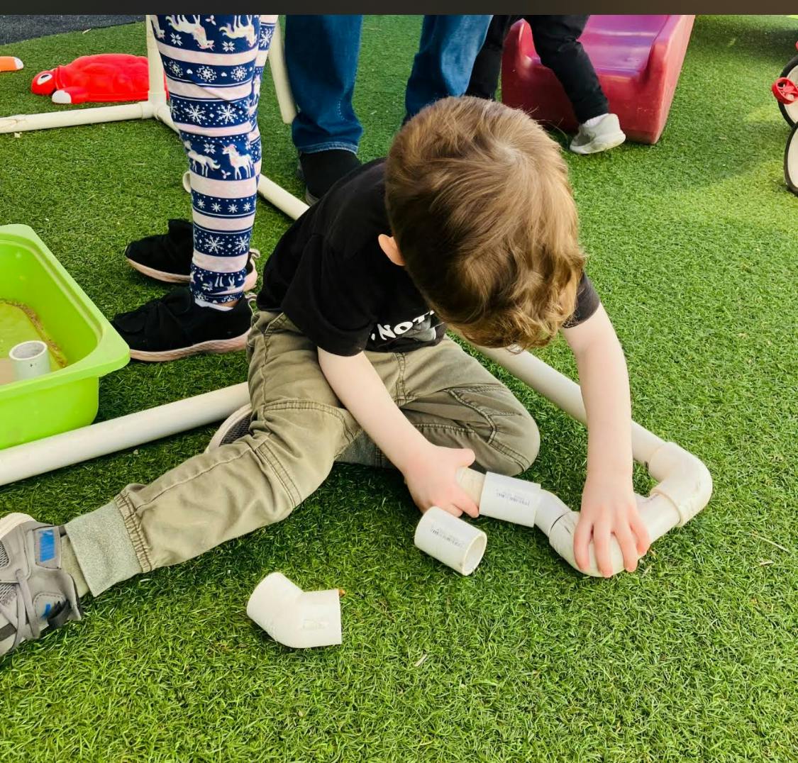 Child on green turf playing with PVC pipes
