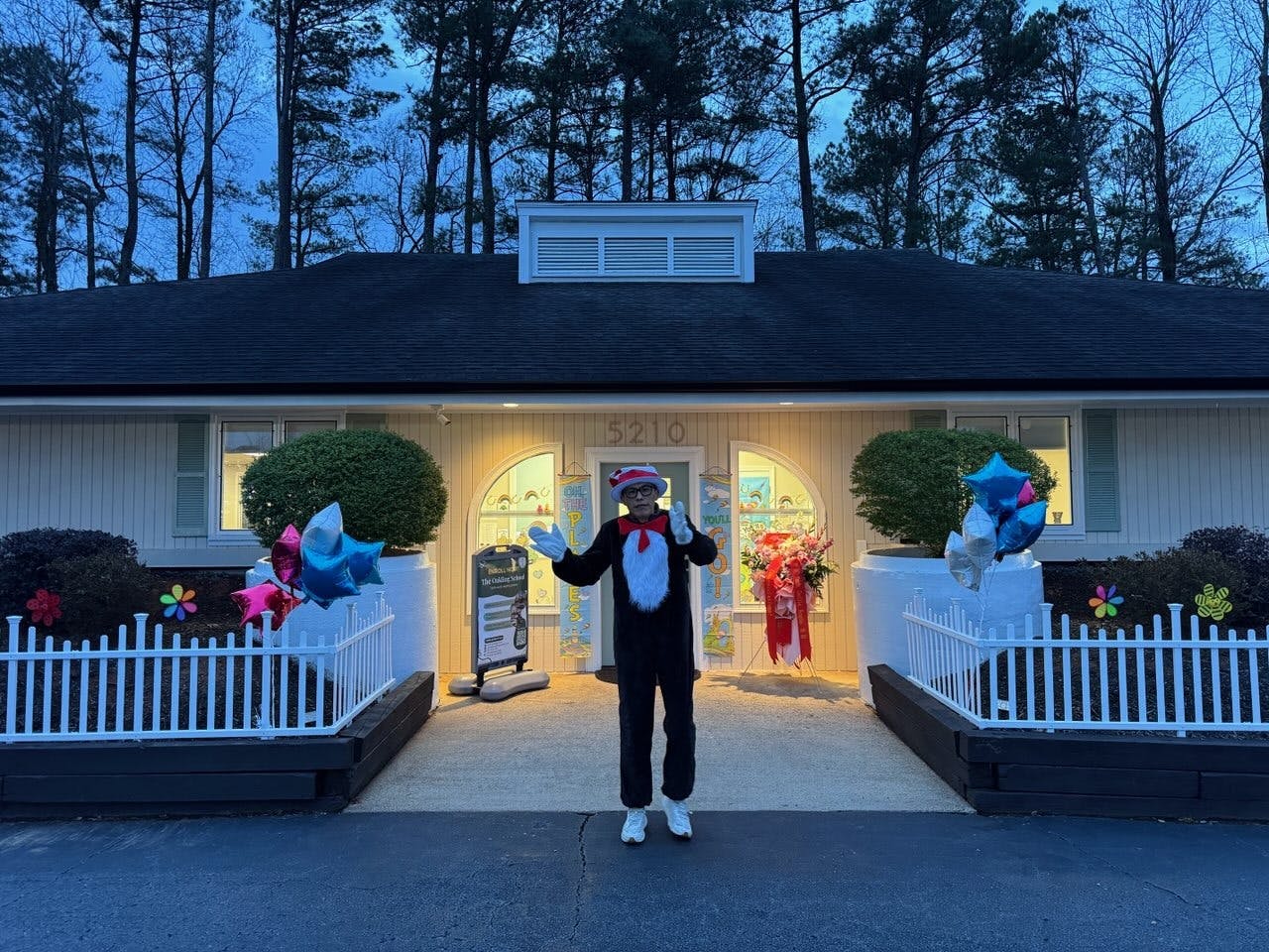Person in a Cat in the Hat costume standing in front of a building with balloons