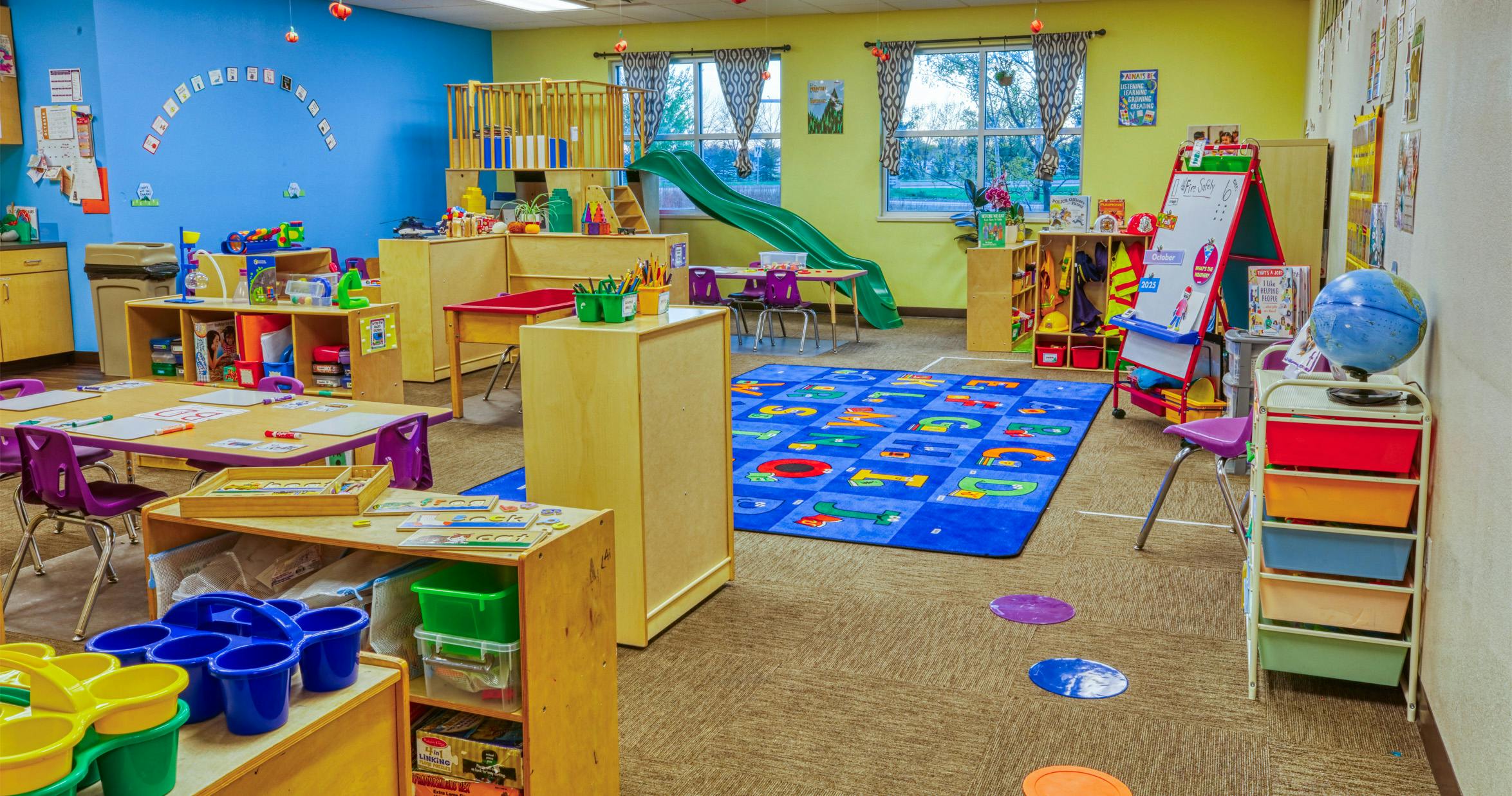A colorful empty preschool classroom with tables, chairs, and play equipment