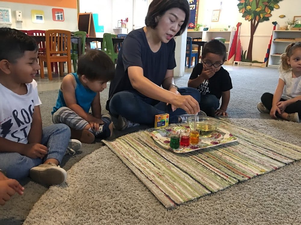 Person and children sitting on floor around tray with colorful liquids