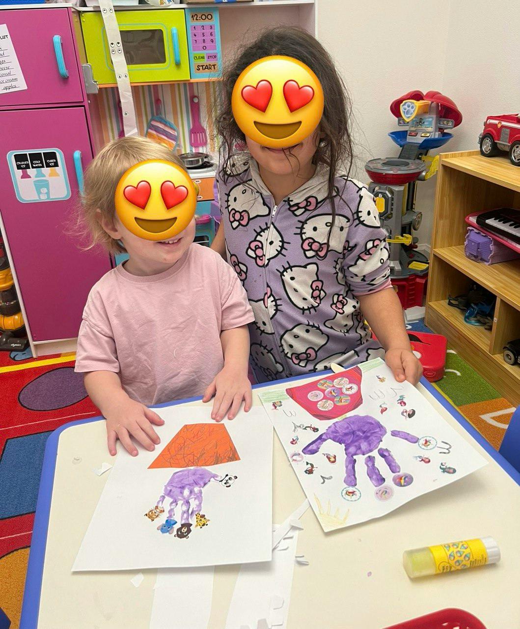 Two children at a table with artwork, showing their handprint artwork