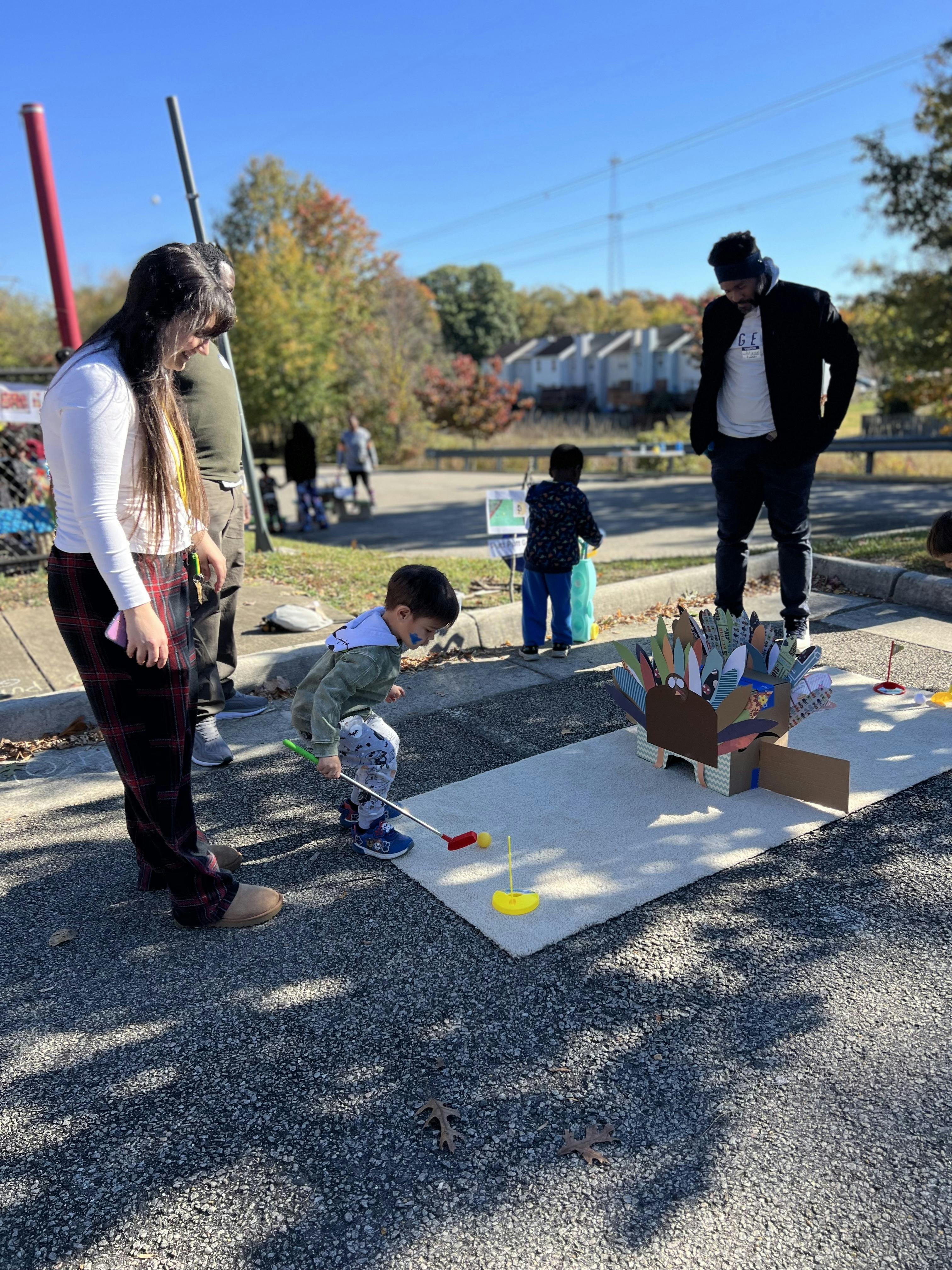 Child playing mini golf with adults nearby