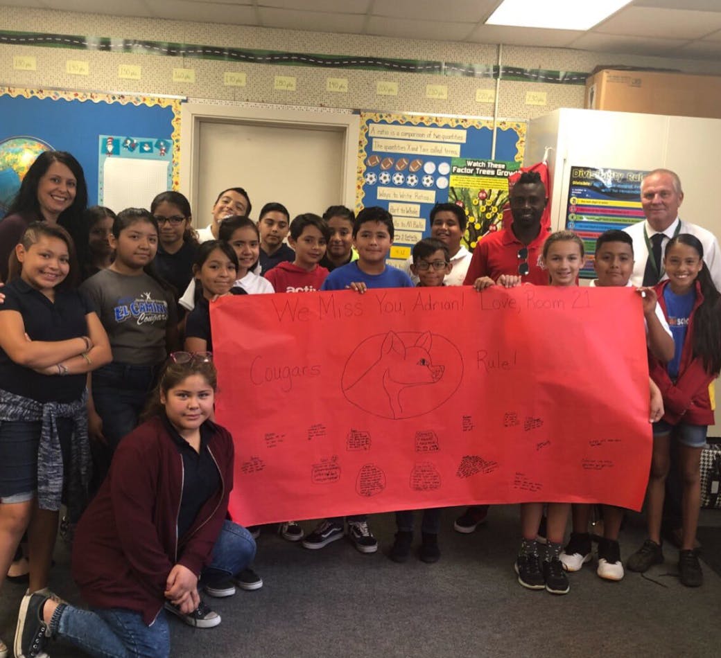 Group of adults and children holding a large red banner in a classroom