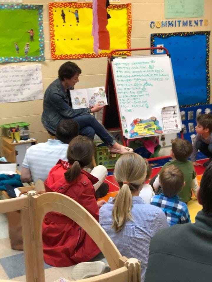 Person reading a book to a group of children in a classroom