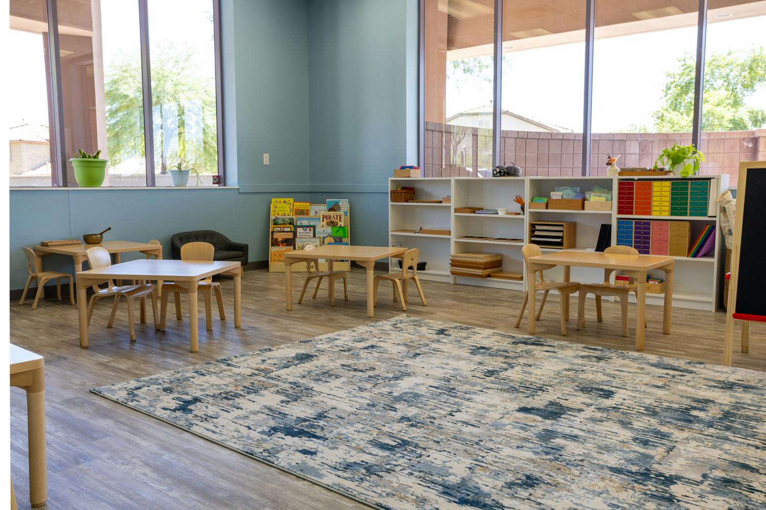 Empty classroom with small tables and chairs, shelves with books and materials