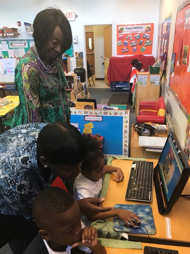 Adults and children looking at a computer in a classroom