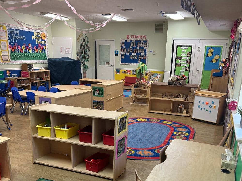A classroom with tables, chairs, shelves, and decorations, including a "Spring Showers Bring Pretty Flowers" board