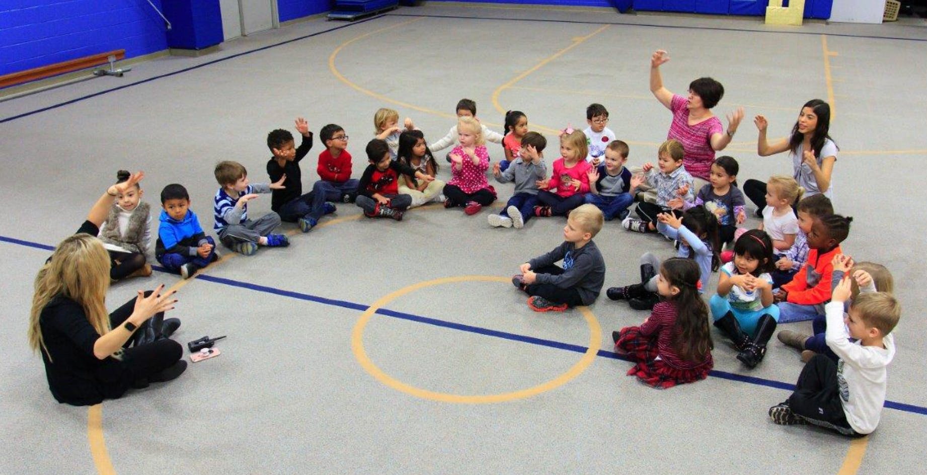 Adults and children sitting in a circle on a gym floor