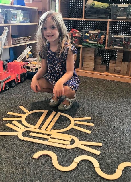Child crouching on floor with wooden blocks arranged in patterns