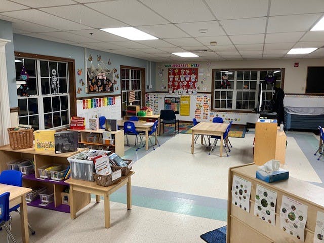 Empty classroom with small tables and chairs, shelves of books and toys