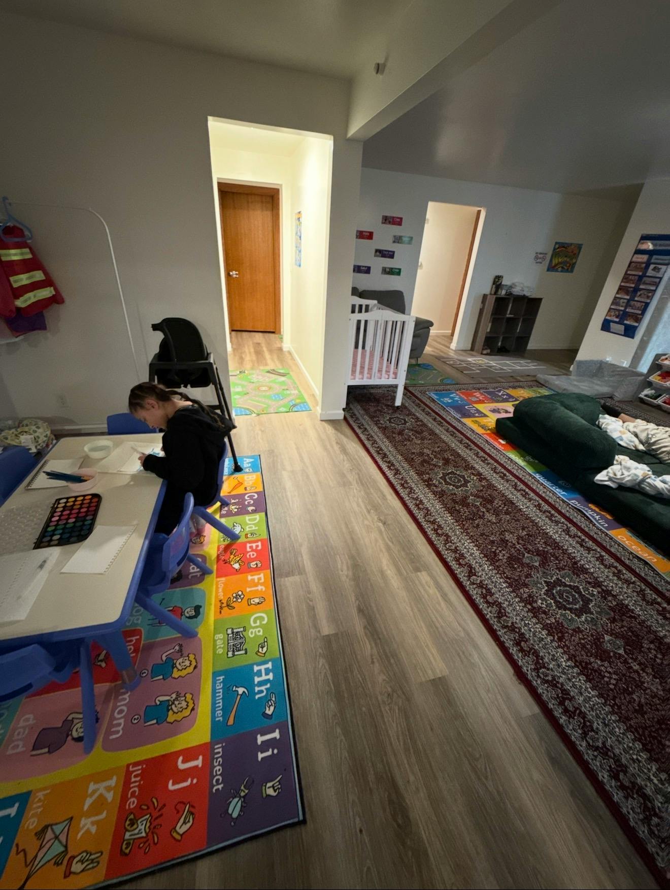 Child drawing at a table with an alphabet rug underneath