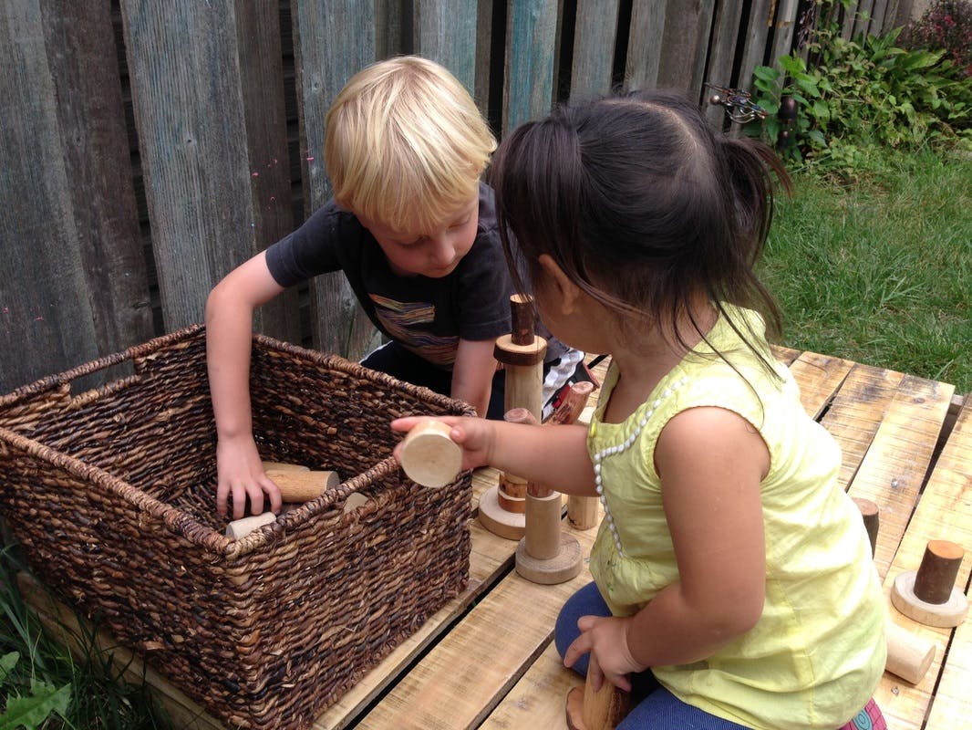 Two children playing with wooden blocks outdoors