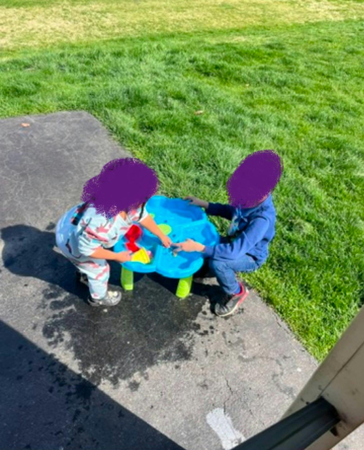 Two children playing with a water table outdoors
