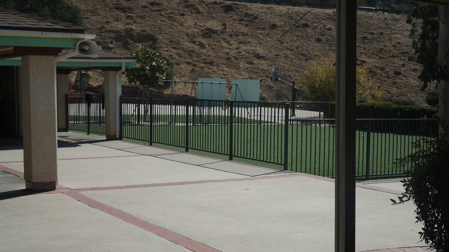 Paved patio area next to a fenced green space with a hill in the background