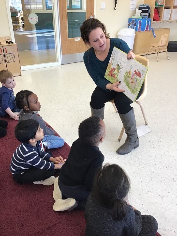 Person reading a book to a group of children in a classroom