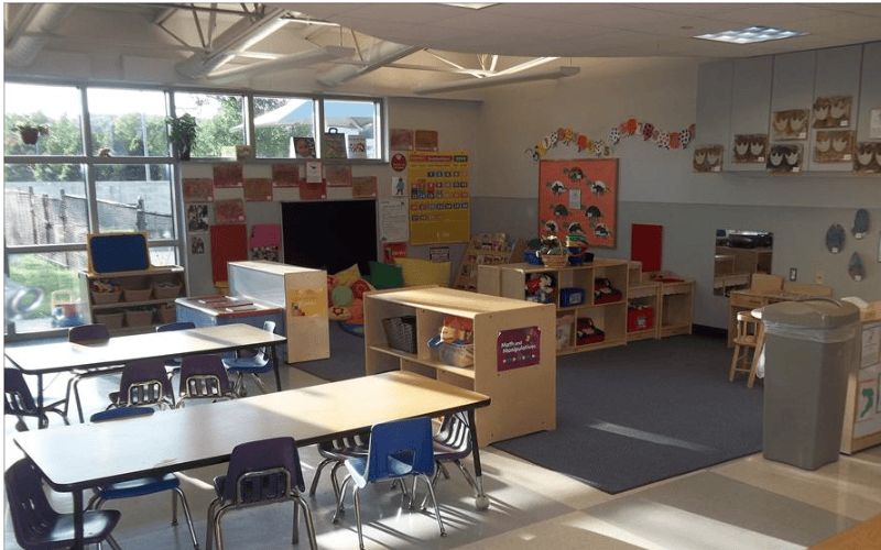 An empty classroom with tables, chairs, and shelves of toys