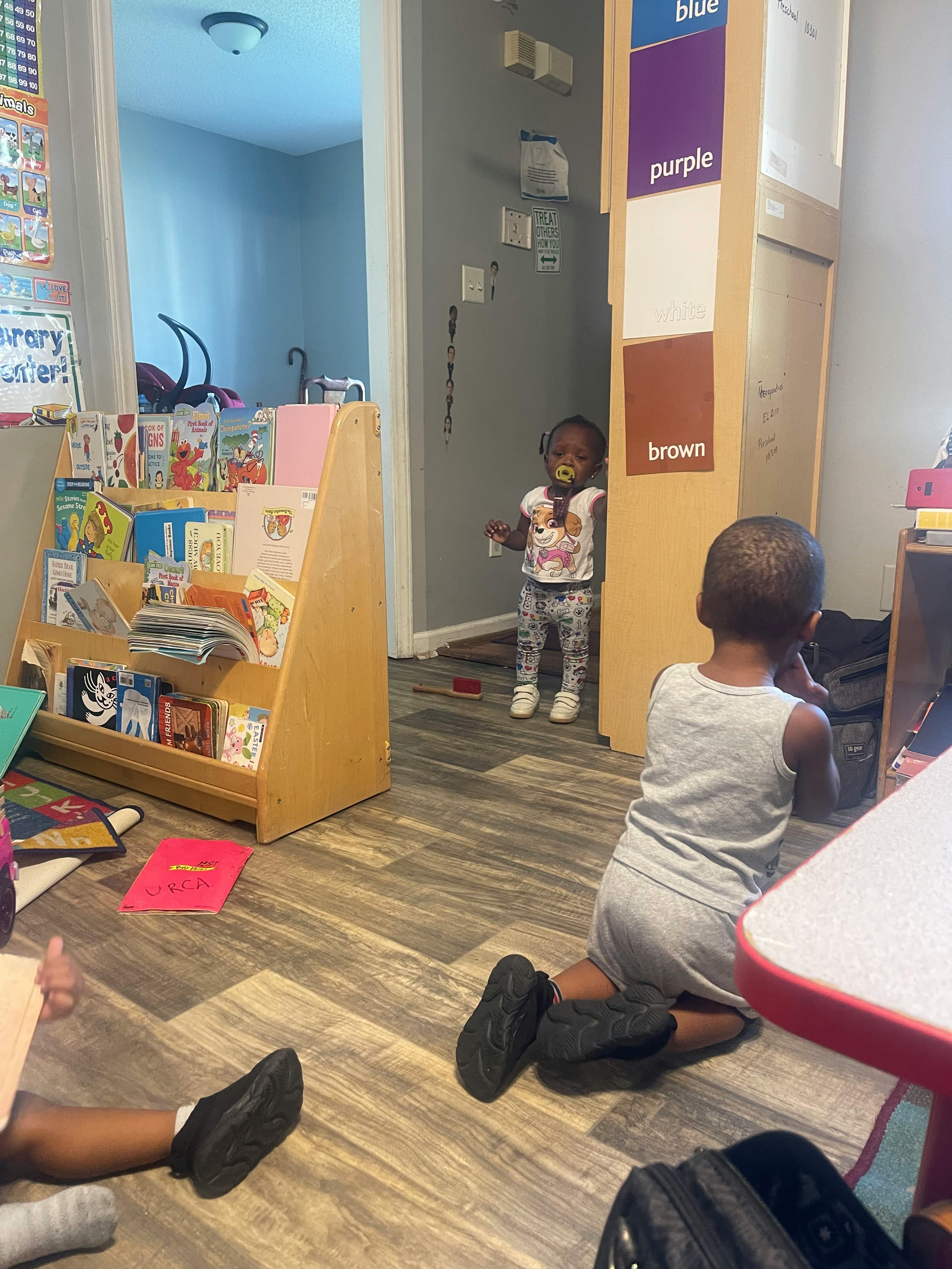 Two children in a room, one standing in a doorway, one kneeling on the floor
