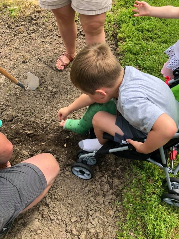 Child with leg cast sitting in stroller, reaching for something on the ground