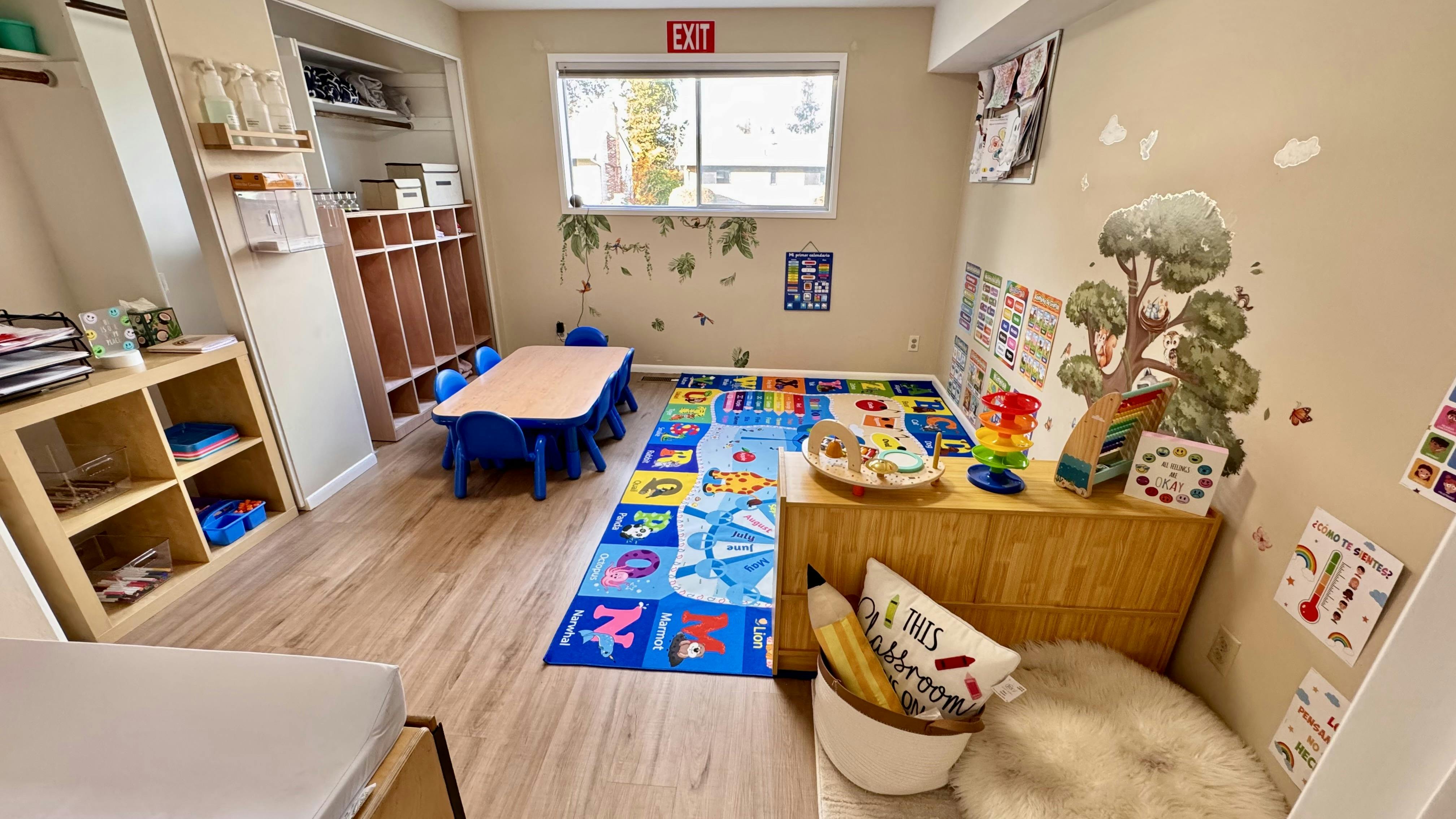 Empty classroom with small table and chairs, colorful rug, and shelves