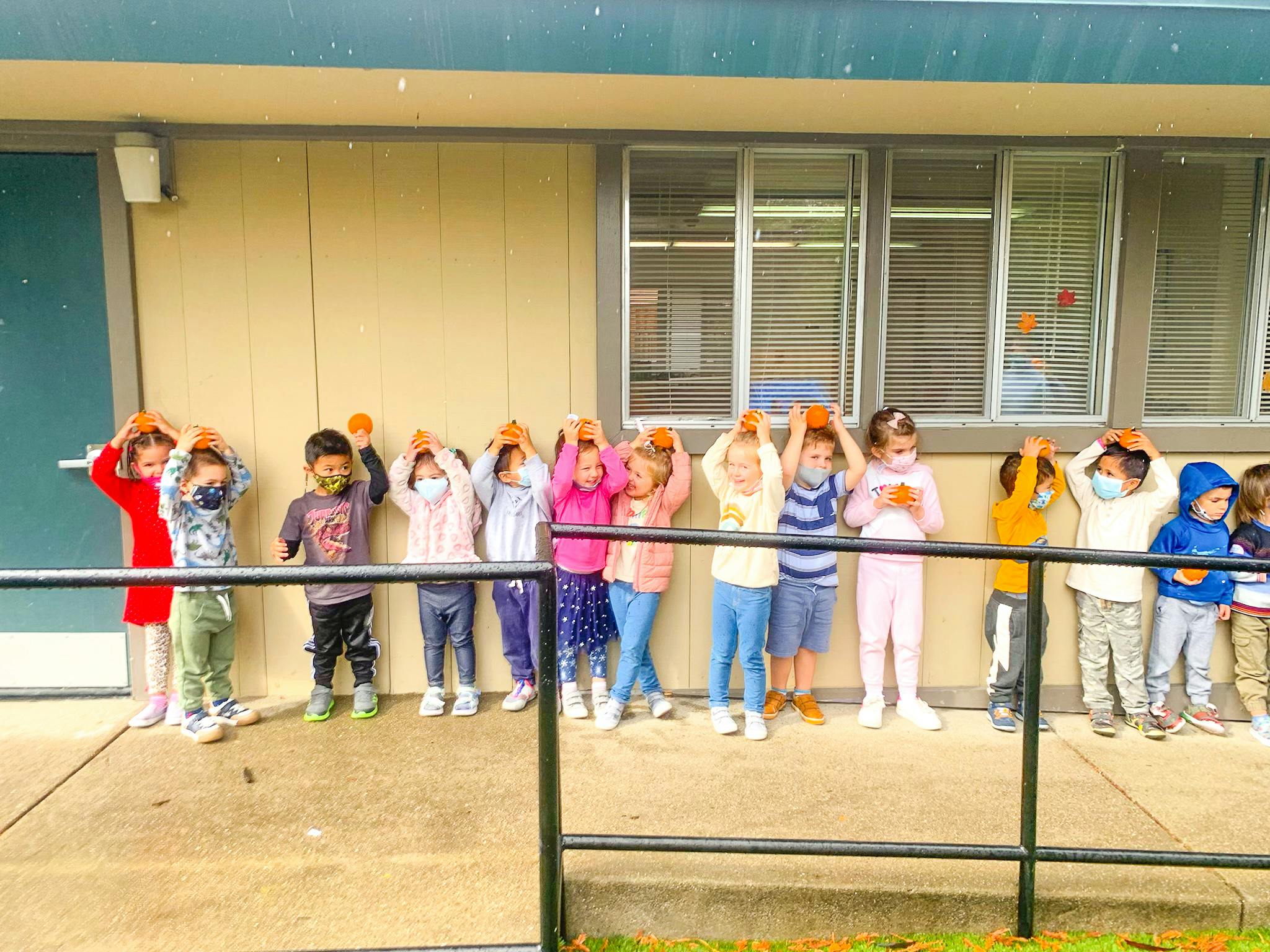 Children standing in a line holding oranges above their heads
