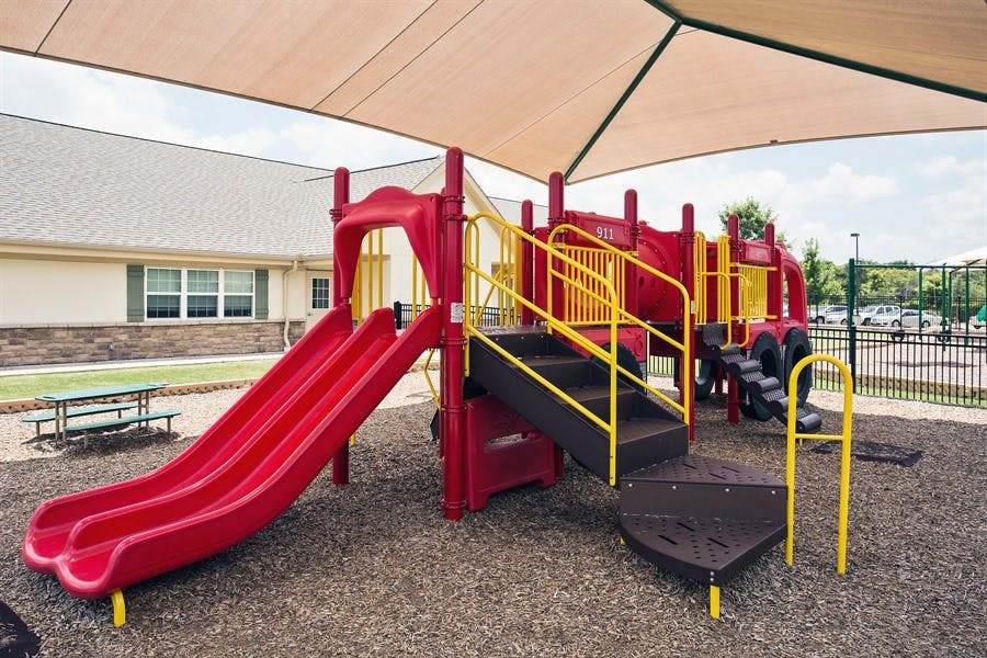 Playground with red slides and yellow railings under a shade canopy