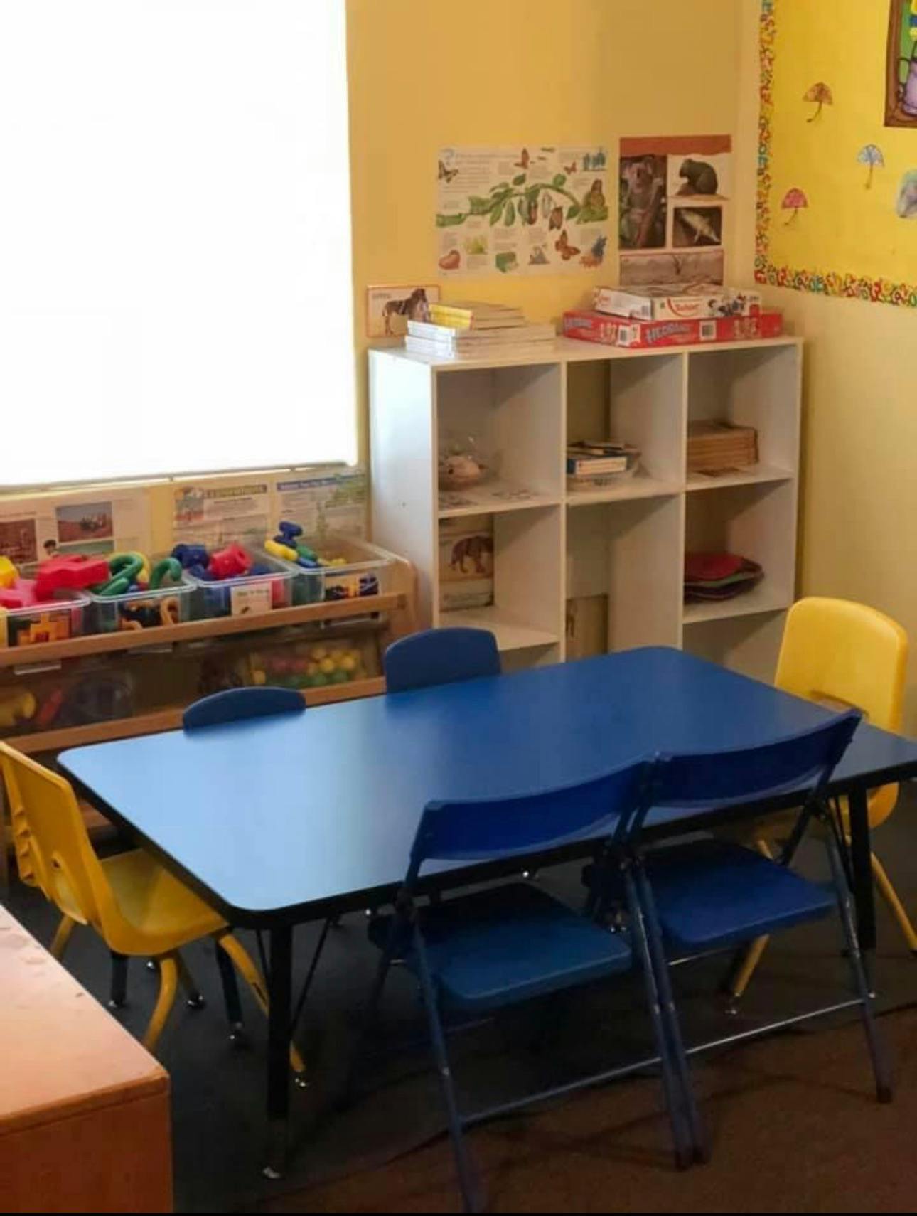 Classroom with blue tables and chairs, and a white storage shelf