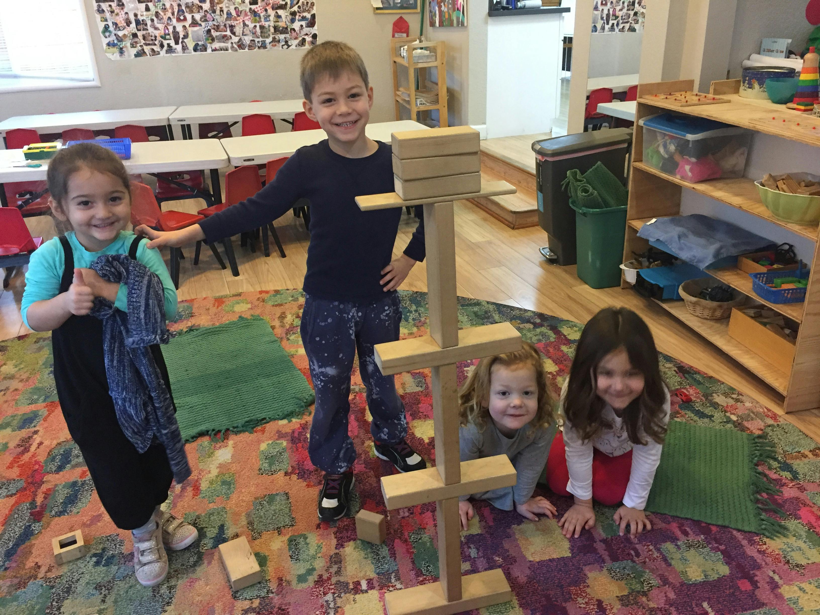 Four children playing with wooden blocks in a classroom