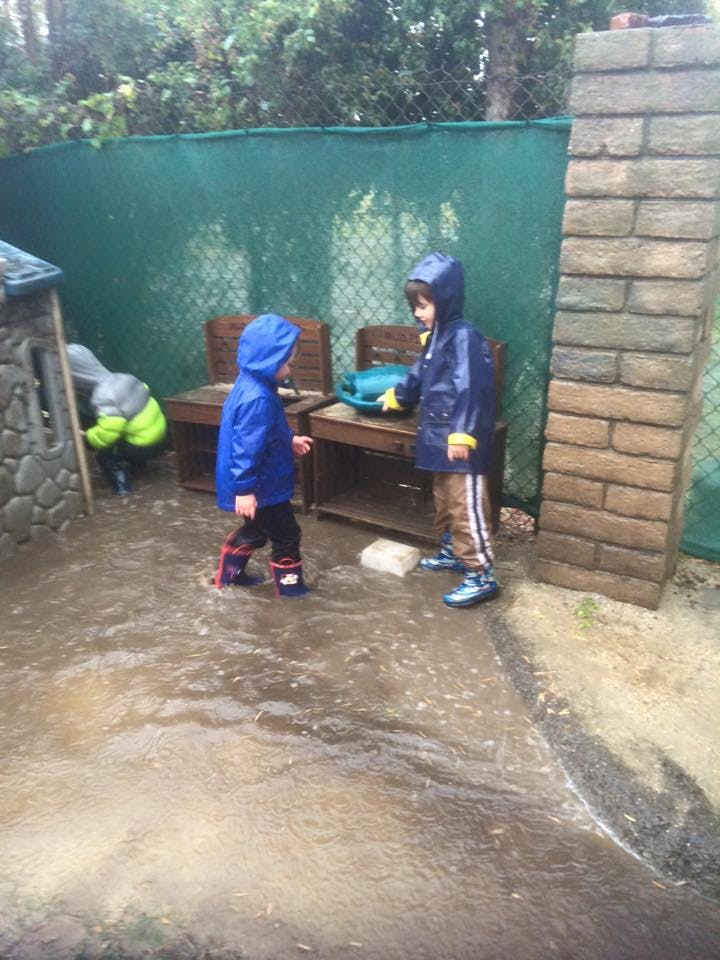 Two children in raincoats standing in a puddle