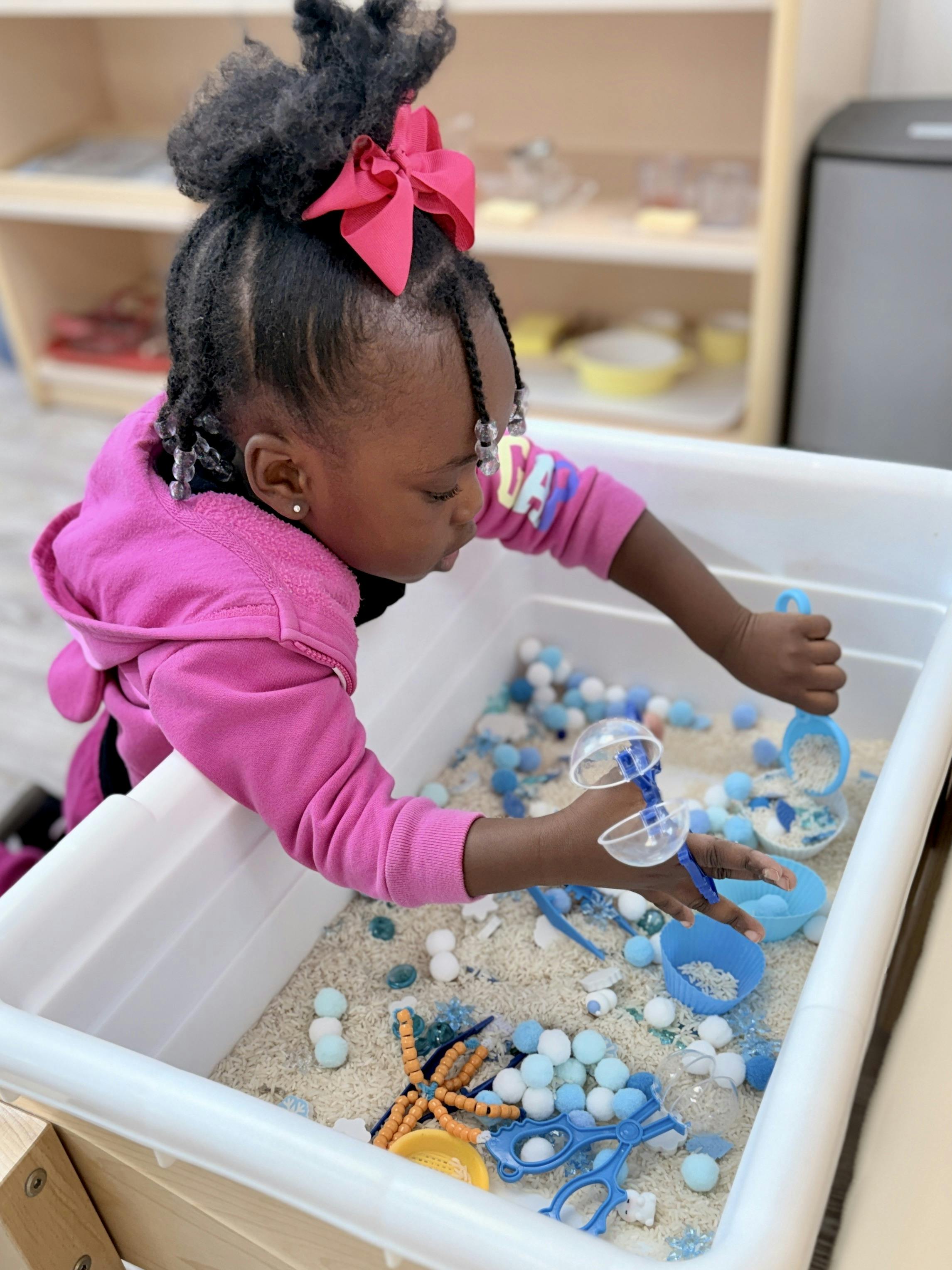 Child playing with rice and small objects in a sensory bin