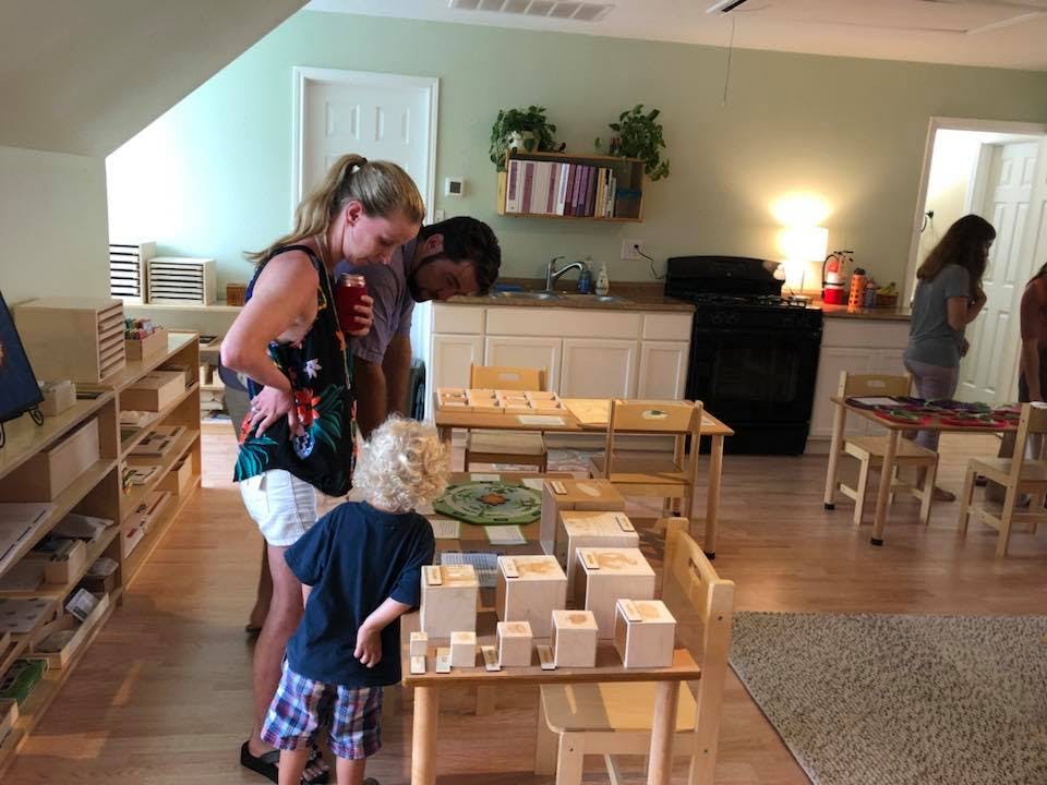 Two adults and a child looking at blocks on a table in a classroom