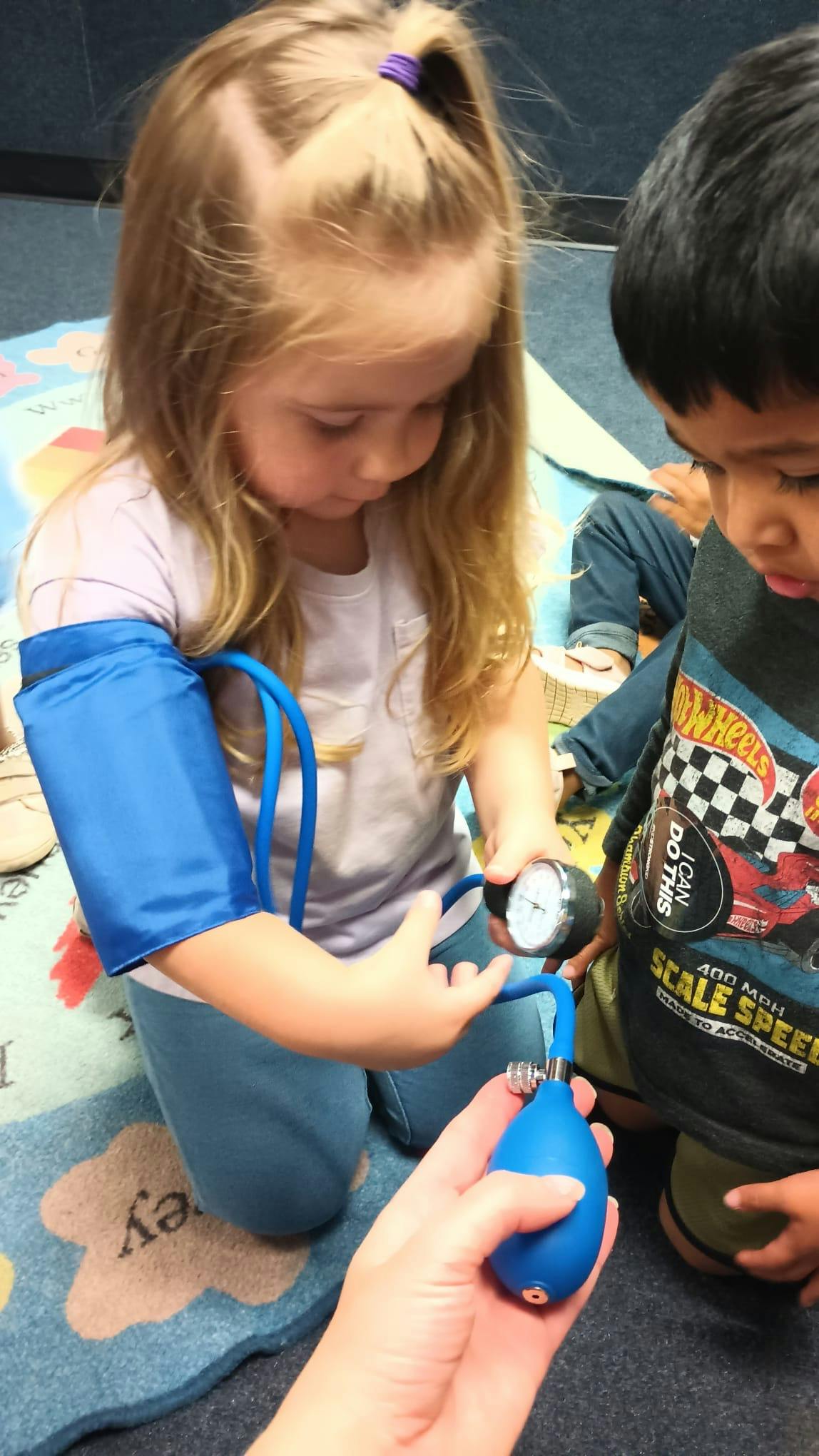Child with a blood pressure cuff on arm, another child watching