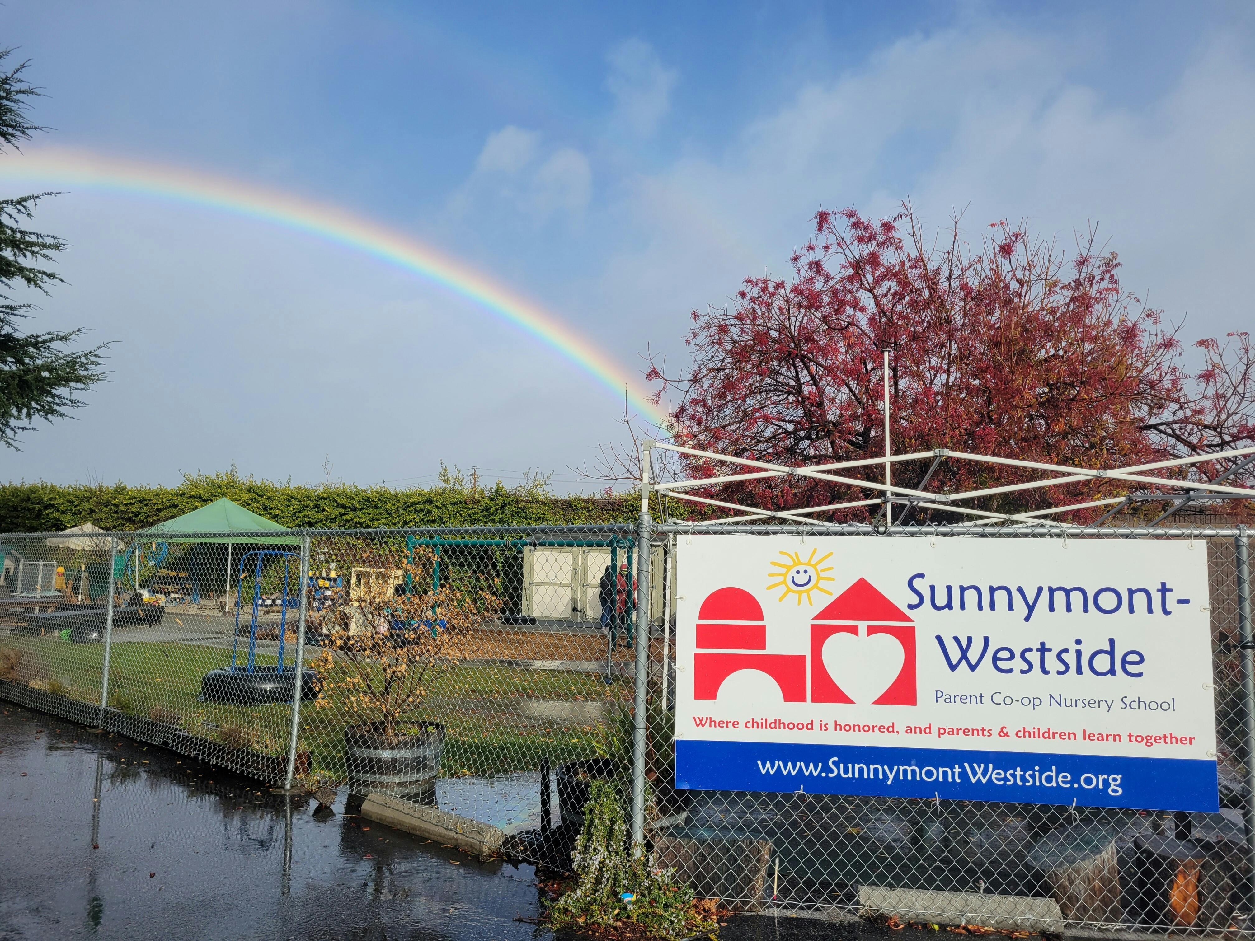 Rainbow over a fenced outdoor area with a sign for Sunnymont-Westside