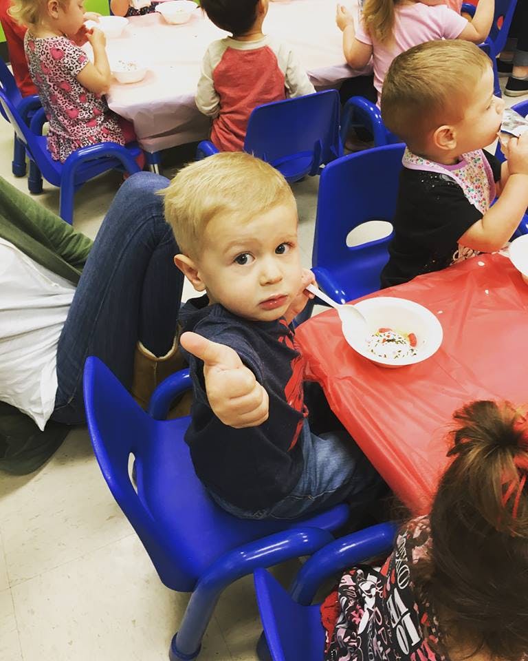 Child giving a thumbs up at a table with other children