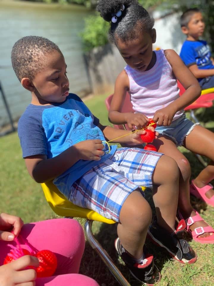 Two children sitting outdoors, one holding a red toy