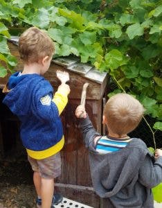 Two children painting a wooden structure outdoors