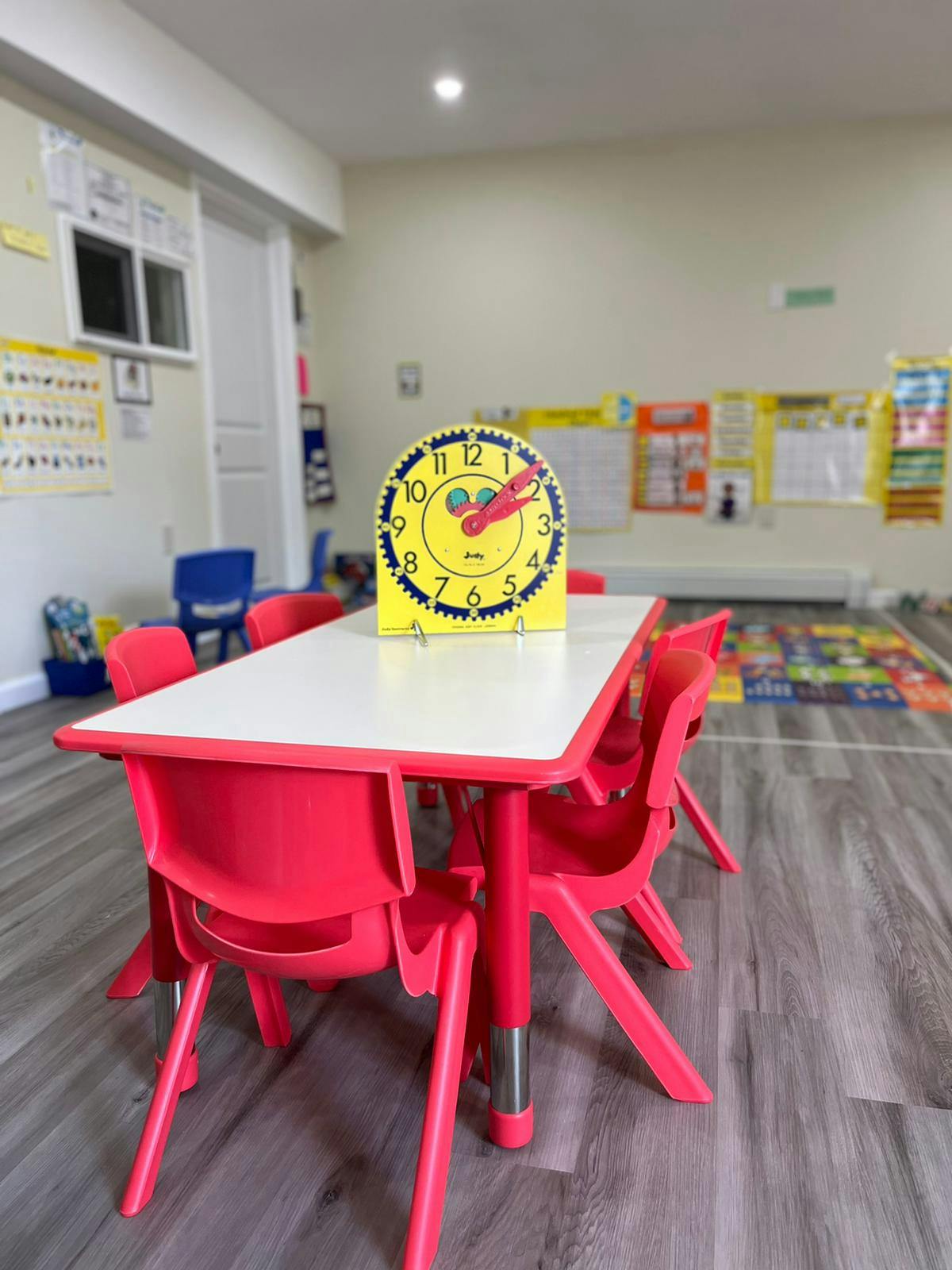 Yellow clock on a white table with red chairs in a classroom