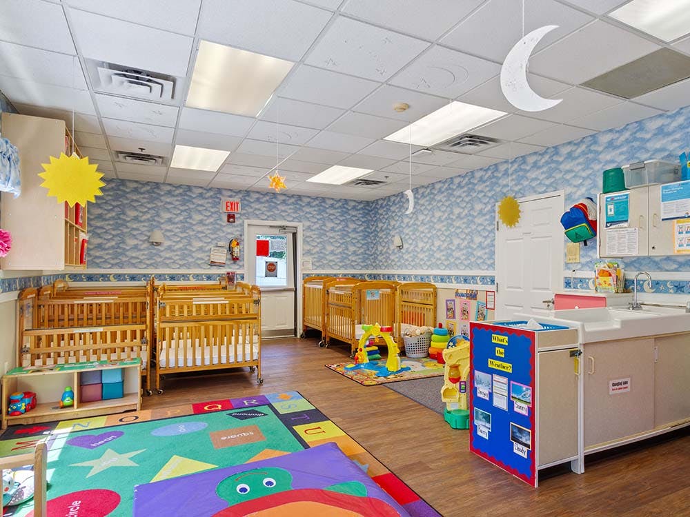 A colorful childcare classroom with cribs, playmats, and a changing station