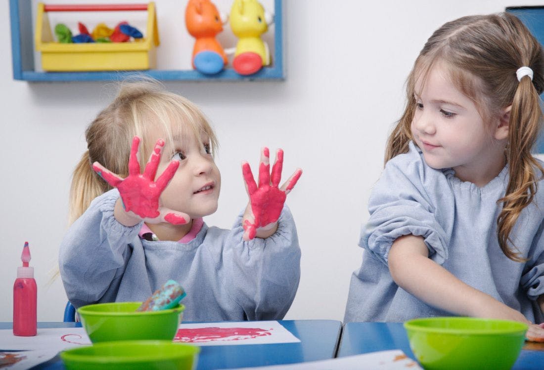 Child with pink paint on hands showing them to another child
