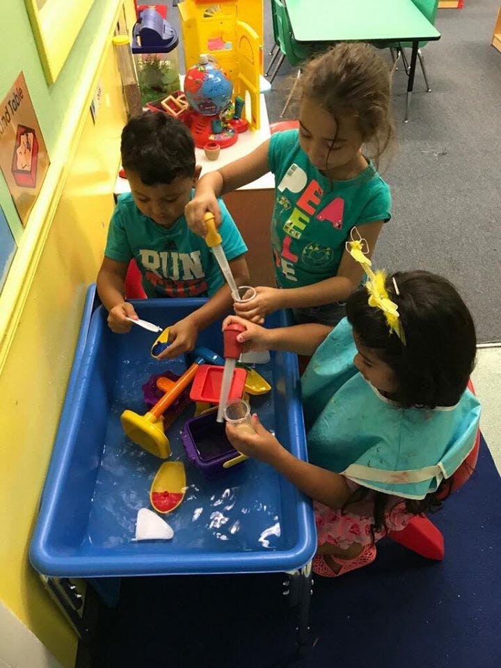 Three children playing with water and toys in a blue sensory bin