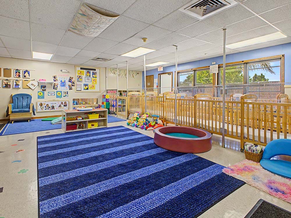 Playroom with cribs, a blue striped rug, and children's toys