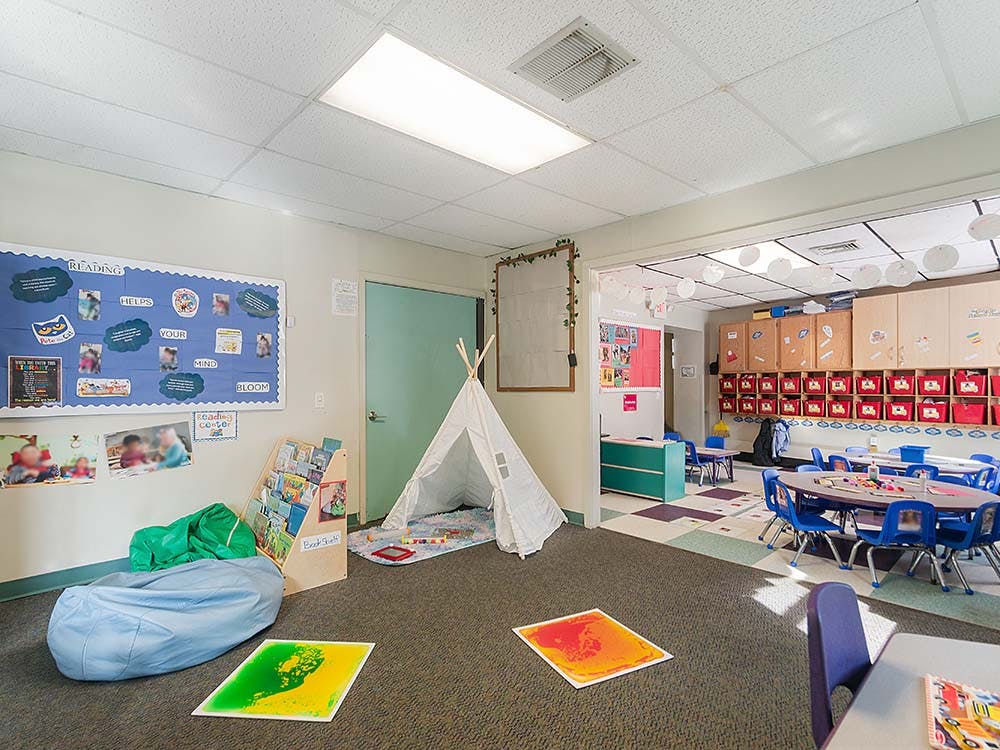 Classroom with children's tables and chairs, a reading nook with a teepee, and bulletin boards