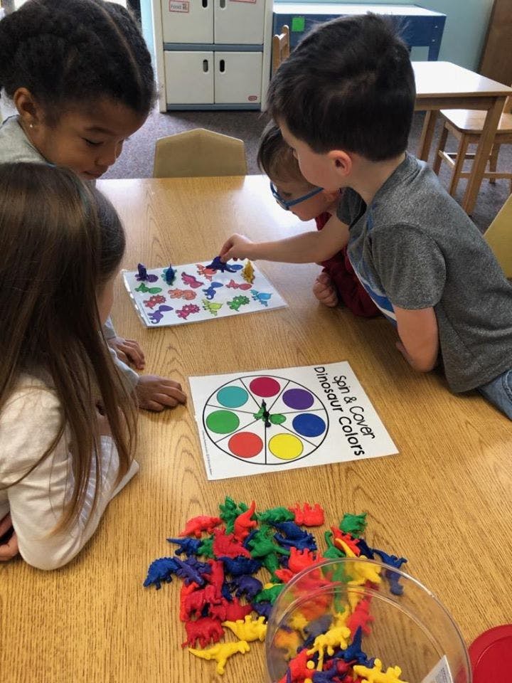 Children playing a game with dinosaur figures and a color spinner