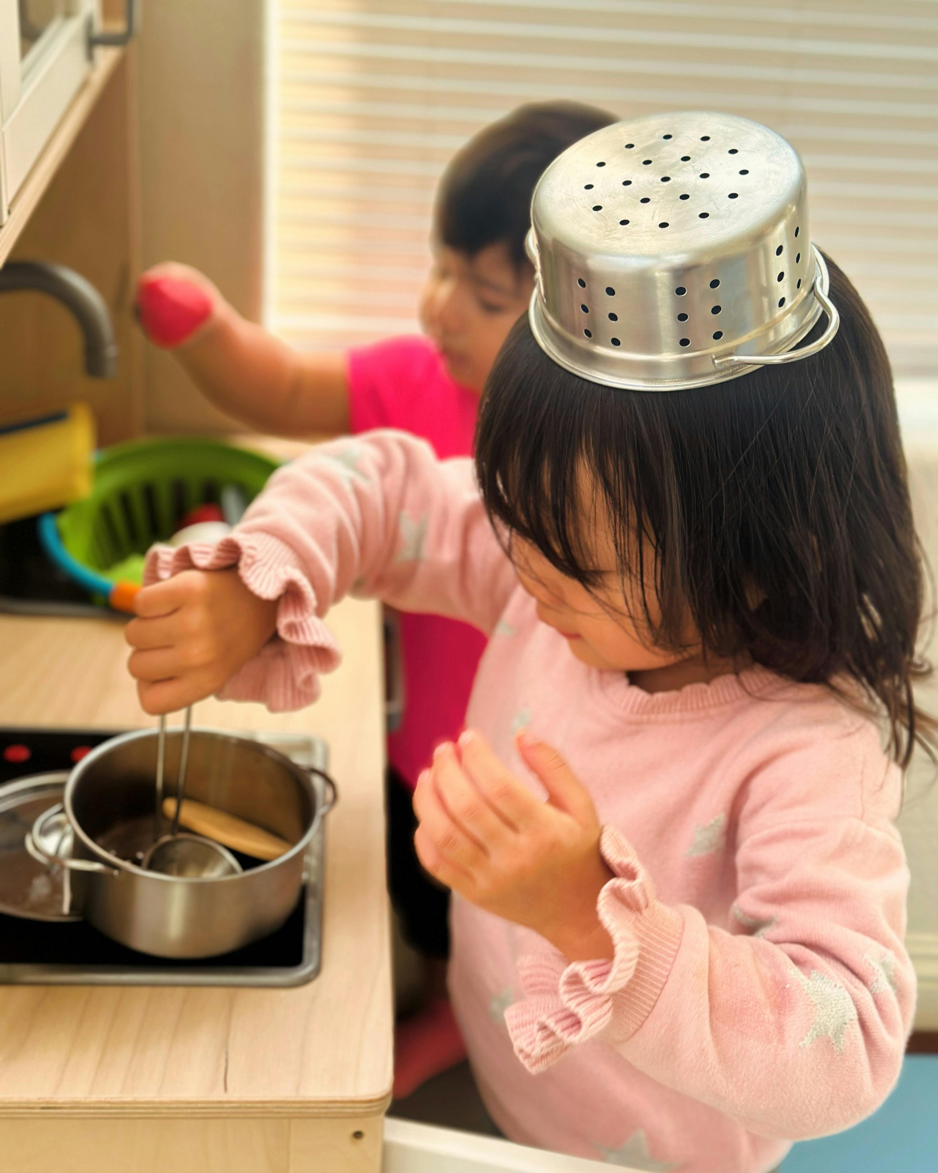 Child with a colander on their head playing with a pot and utensils
