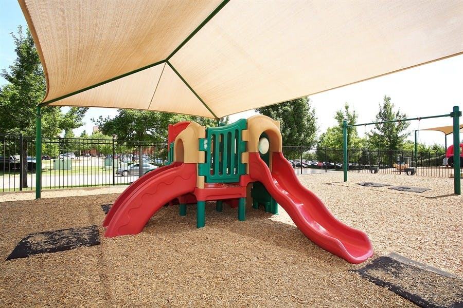 Playground with red and tan slides under a large shade canopy