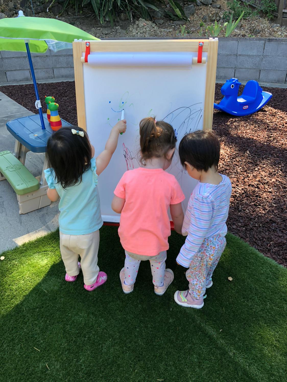 Three children drawing on an easel outdoors