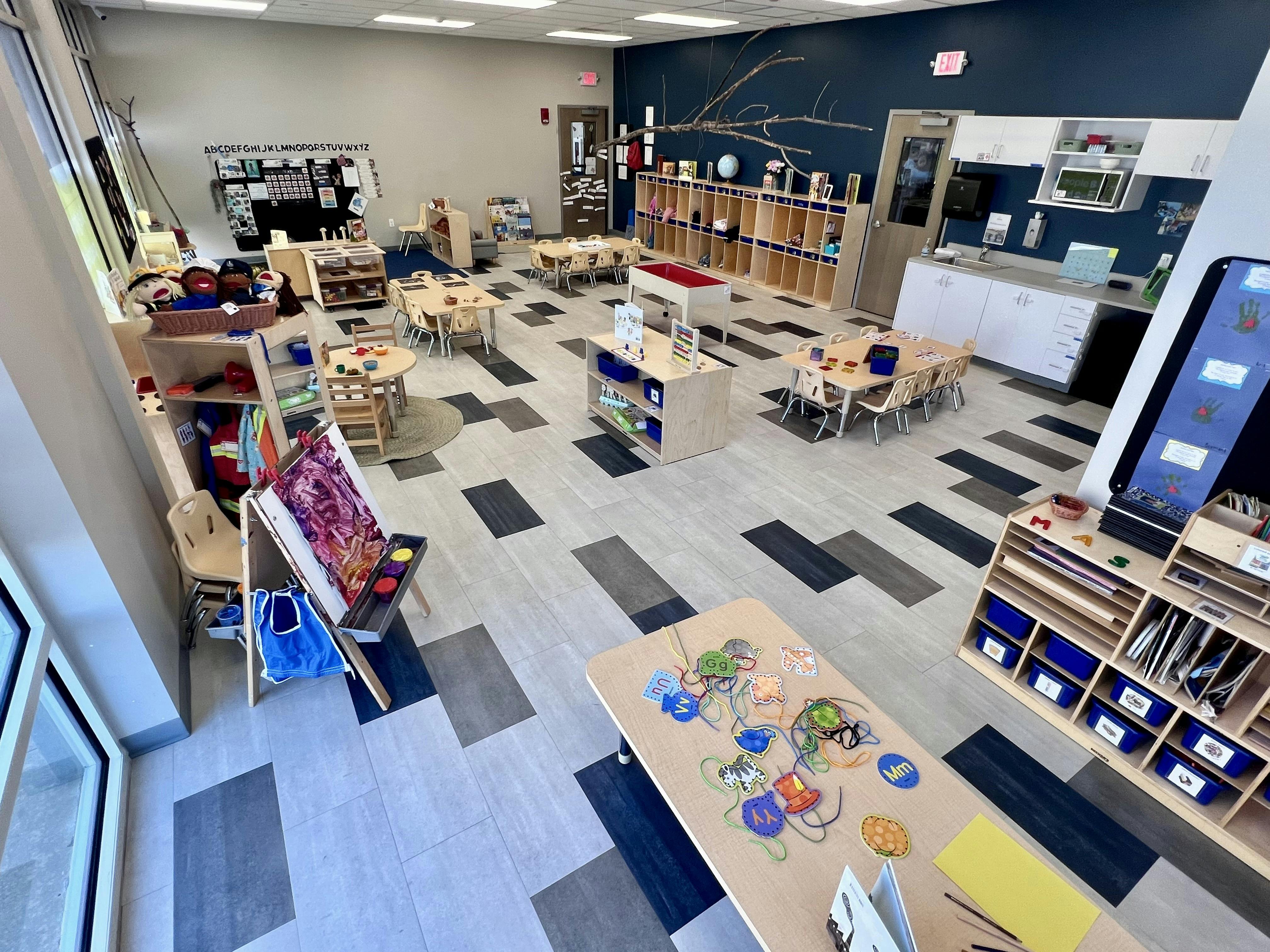 Classroom with small tables and chairs, shelves, and an easel