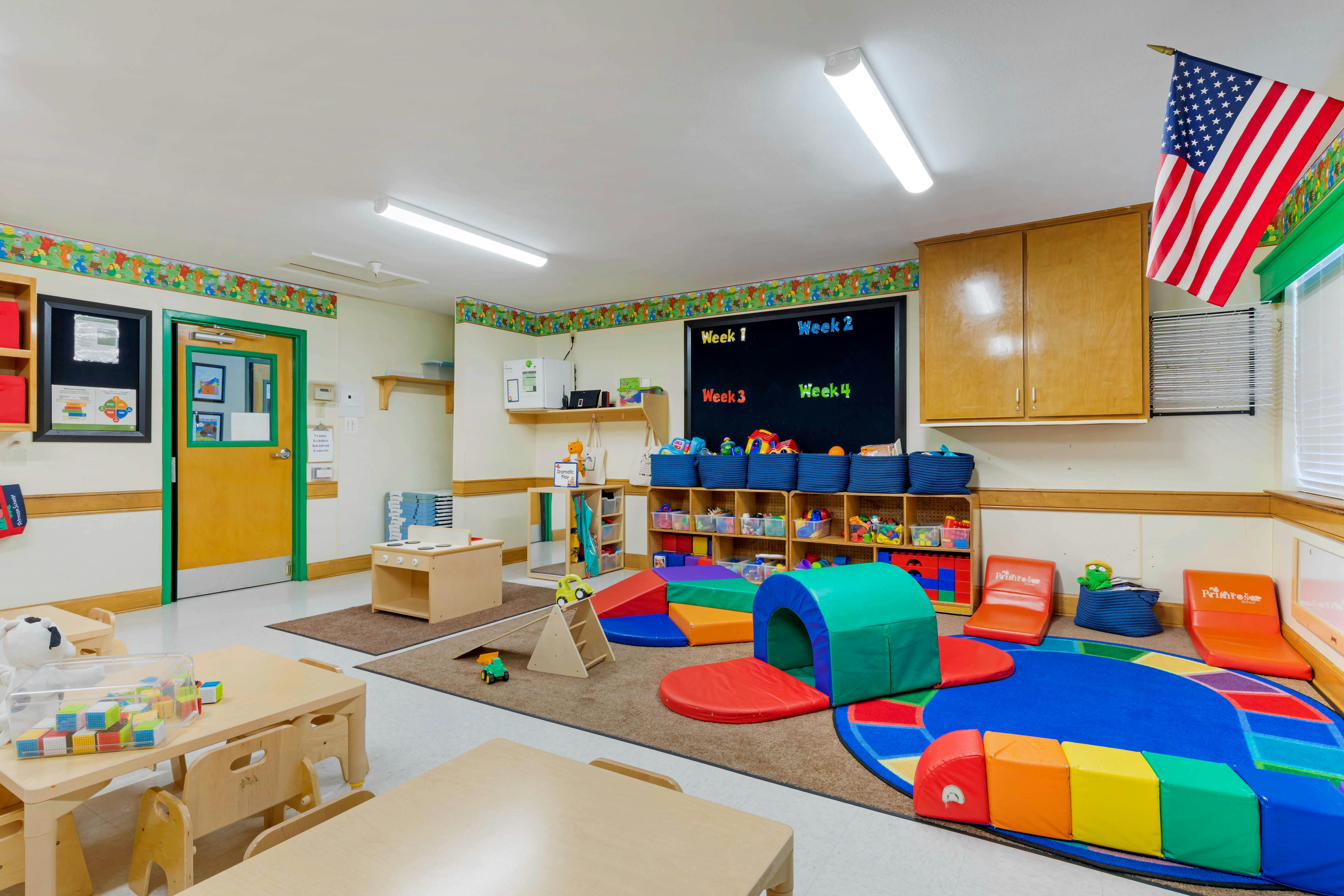 Children's classroom with small tables, play mats, and storage shelves