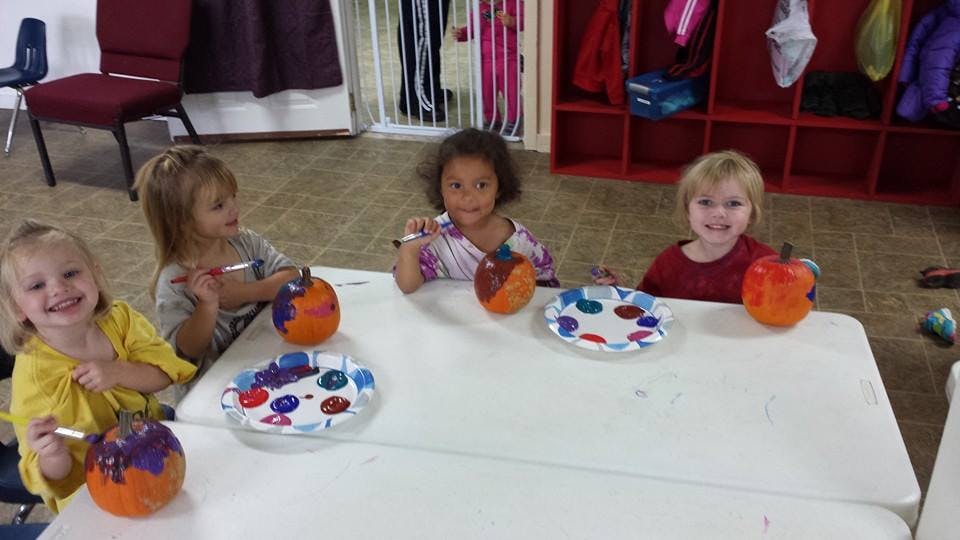 Four children painting pumpkins at a table